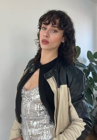 Veste bomber en cuir avec des panneaux beige et noir sur une robe à sequins argentée. L'ensemble présente une coupe cintrée et un col rond.