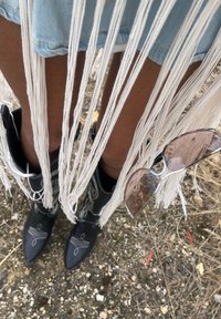 Črne kavbojske čevlje s koničastimi prsti in belimi dekorativnimi šivi, v kombinaciji s svetlo jeans krilom, ki ima dolge bele frinže.
