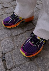 Purple and black sports shoes with orange and yellow accents, featuring mesh fabric, textured soles, and reflective detailing.