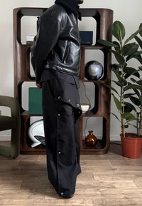 Veste en cuir noir avec col en shearling, associée à un pantalon large noir avec poches et accents en métal argenté.