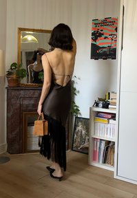 Braunes Satin-Kleid mit rückenfreiem Design und fransensaum. Person hält eine kleine braune Handtasche mit minimalistischem Stil.