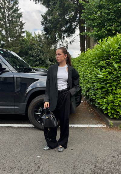 Blazer negro de gran tamaño sobre una camiseta blanca, combinado con pantalones anchos negros y mocasines a cuadros. Sosteniendo un pequeño bolso negro.