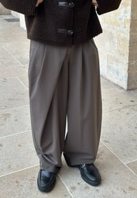 Brun fleecejakke med svarte knappedetaljer, kombinert med løse, høytlivde grå bukser og klumpete svarte platåsko.