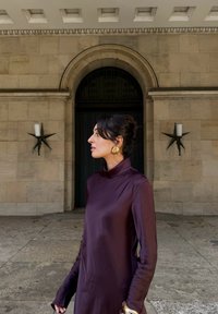 Abito a maniche lunghe con collo alto in seta viola scuro, caratterizzato da una vestibilità morbida. Orecchini circolari dorati e parete texturizzata con applique a forma di stella.