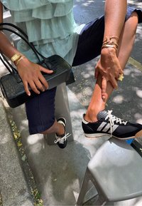 Chaussures de sport noires avec accents blancs et lacets blancs. Portées avec un pantalon court bleu marine. Haut vert clair texturé et superposé. Sac à main noir.