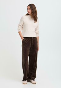 Hnedé kordové nohavice so širokým strihom, elastickým pásom a šnúrkou. V kombinácii s krémovým svetrom a teniskami.