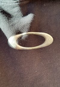 Črn material z metalno srebrnim ovalnim akcentom. Tekstura je gladka z rahlim sijajem, kar kontrastira z mat površino.