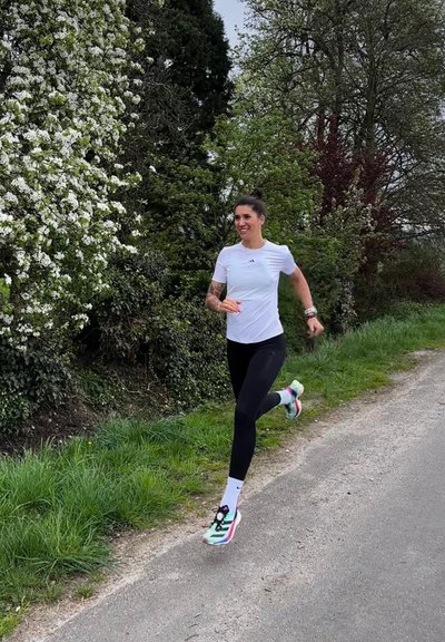 Camiseta atlética blanca, leggings negros y zapatillas de running coloridas con acentos en aqua, rosa y negro. Rodeado de follaje verde y flores.