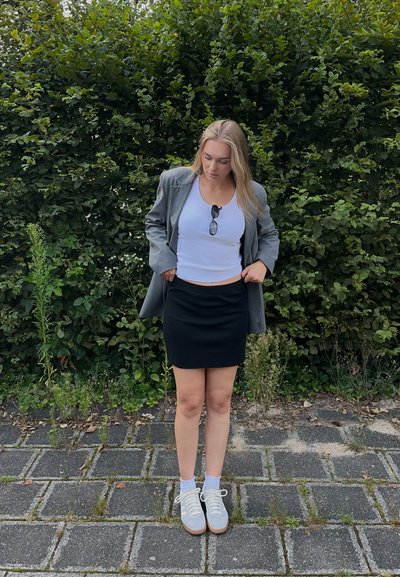 Blazer gris, top corto blanco, falda negra y zapatillas blancas con suelas de colores claros. Gafas de sol descansando sobre el blazer.