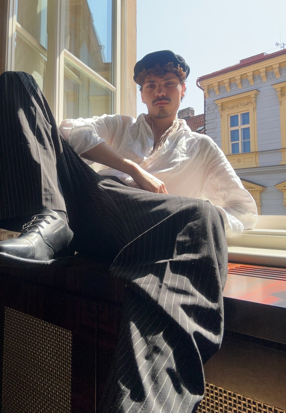 Zwart-witte gestreepte broek, wit shirt en zwarte baret. Zittend bij een raam met zonlicht, toont een gecombineerd gebruik van texturen en lagen.