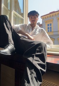 Zwart-witte gestreepte broek, wit shirt en zwarte baret. Zittend bij een raam met zonlicht, toont een gecombineerd gebruik van texturen en lagen.