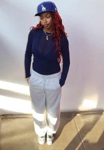 Camiseta de manga larga en color navy, superpuesta sobre una tela transparente, combinada con pantalones de chándal en gris claro y zapatillas blancas. Una gorra de béisbol completa el look.