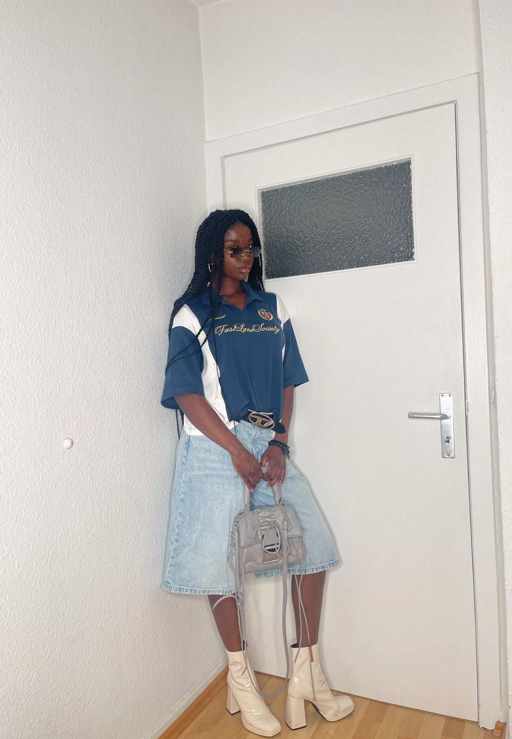 Blau-weiße oversized Poloshirt mit Logo, hellblaue Jeansrock, be beigefarbenen Knöchelschuhen und einer kleinen grauen Handtasche mit Tragegurt.