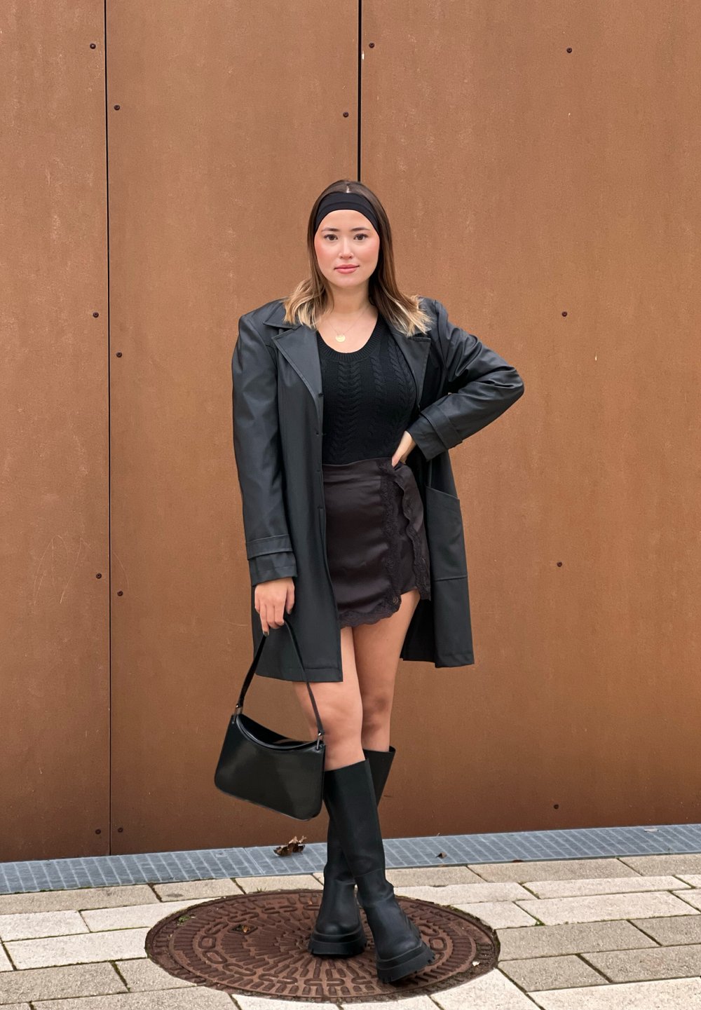 Μαύρο ψεύτικο δερμάτινο παλτό πάνω από ένα μαύρο πουλόβερ με πλέξεις και μια μαύρη φούστα με δαντέλα. Συνδυασμένο με μαύρες ψηλές μπότες και μια μικρή μαύρη τσάντα.