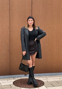 Μαύρο ψεύτικο δερμάτινο παλτό πάνω από ένα μαύρο πουλόβερ με πλέξεις και μια μαύρη φούστα με δαντέλα. Συνδυασμένο με μαύρες ψηλές μπότες και μια μικρή μαύρη τσάντα.