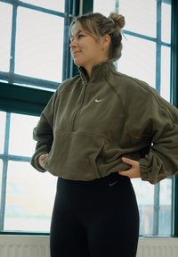 Polaire verte à col montant, zip partiel et poche avant ; associée à des leggings taille haute noirs avec un petit logo.