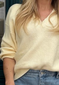 Sweater de malha amarelo claro com decote em V e mangas soltas, combinado com calções de ganga de cintura alta. Detalhe de nervuras texturizado visível.