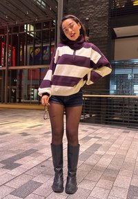 Ylimittaiset viininpunavalkoraidalliset fleece-poolopaita korkealla kauluksella, yhdistetty farkkushortseihin ja korkeisiin mustiin saappaisiin. Käsissä pidettävät kirkkaat silmälasit.