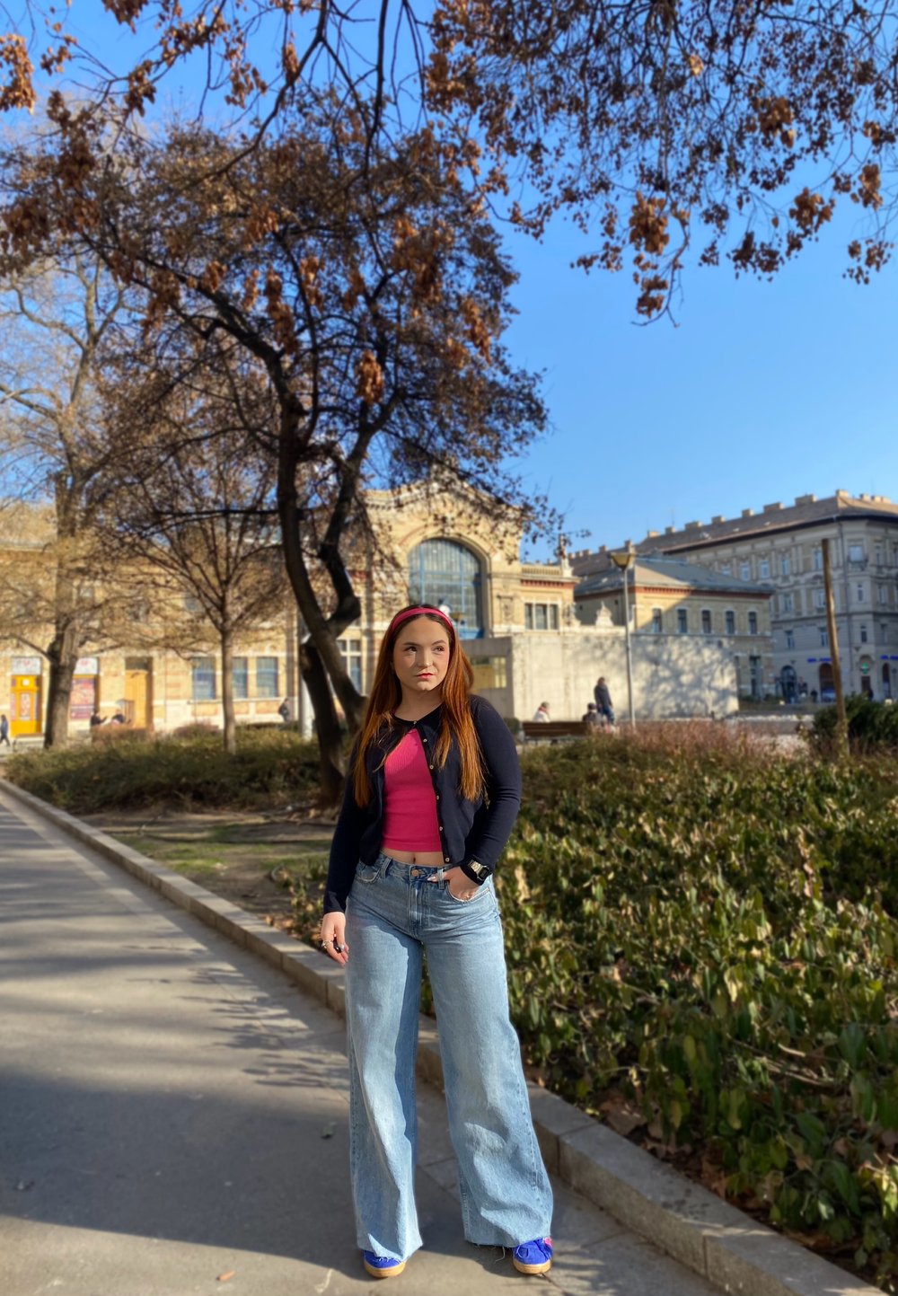 Jeans a zampa d'elefante di colore azzurro chiaro, top rosa e cardigan blu navy; ambiente all'aperto con alberi e un edificio storico sullo sfondo.