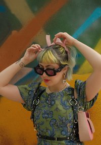 Φλοράλ πράσινο φόρεμα με φουσκωτά μανίκια, μαύρος ιμάντας με ασημί δακτυλίδια, ροζ τσάντα χεριού, γυαλιά ηλίου, κορδέλες μαλλιών και περιδέραιο με πέρλες.