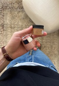 Hånd, der holder to hudplejebeholdere: Clinique Moisture Surge og UpCircle Eye Cream, med blå jeans og sort top synlig.