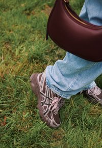 Sportcipők barna és fekete kockás mintával, szürke részletekkel és textúrázott talppal, világoskék farmerrel és bordó táskával párosítva.