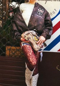 Braune Leder-Bomberjacke mit Adidas-Logo, rote Spitzensleggings und eine Schlangenleder-Handtasche mit Augendetail und strukturierter Oberfläche.