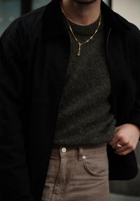 Black corduroy jacket, olive green jumper, light brown high-waisted trousers, gold chain necklace, textured materials, simple design.