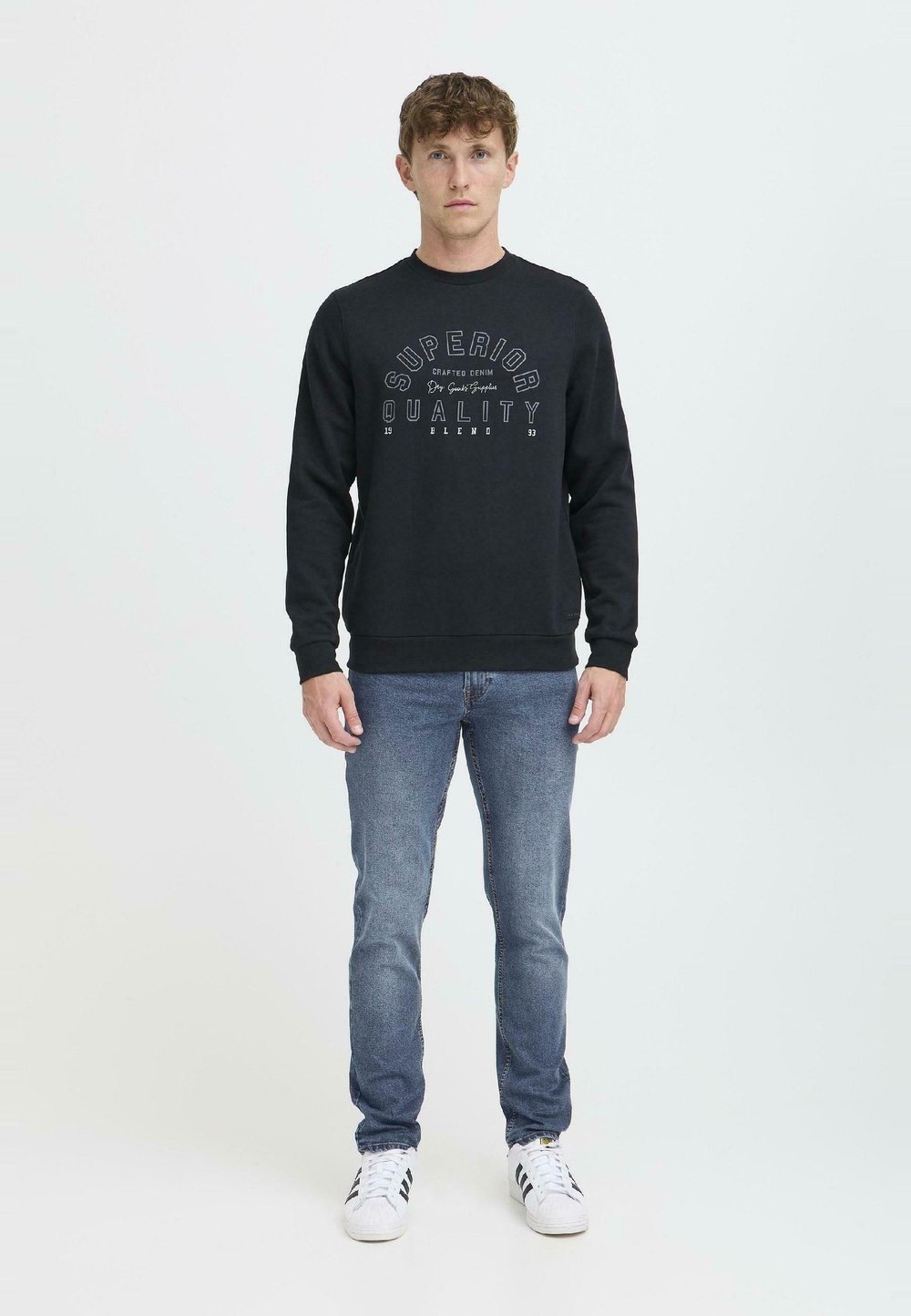 Black sweatshirt featuring "SUPERIOR QUALITY" printed in white, with a crew neck and ribbed cuffs. Styled with blue jeans and white trainers.