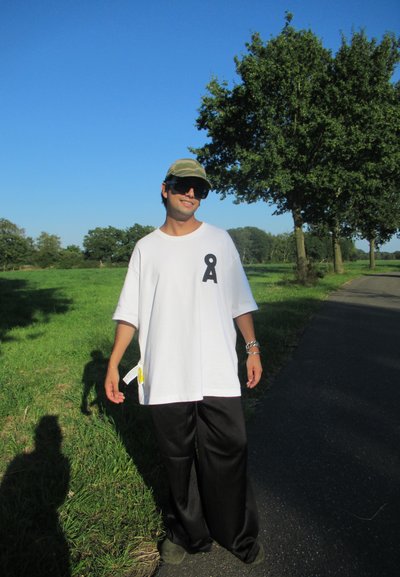 Camiseta blanca de gran tamaño con un gráfico negro, combinada con pantalones anchos negros. Una gorra verde y unas gafas de sol grandes completan el look.