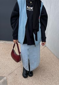 Τζιν γιλέκο σε ανοιχτό μπλε απόχρωση πάνω από μαύρη φανέλα με λογότυπο "NIKE"; μαύρη φούστα με μπροστινή σχισμή; μαύρες μπότες μέχρι τον αστράγαλο; κόκκινη τσάντα.