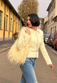 Helles gelbes Zip-up Sweatshirt mit Kragen und Gürtel, kombiniert mit blauen Jeans und einer flauschigen Handtasche in kremfarbener Farbe.