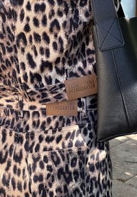 Leopardimustriga kangas beeži ja musta värvigammaga pükstel; omaduseks pruunist nahast sildid "BAUM UND PFERDGARTEN." Läheduses must kott.