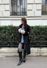 Črni volneni plašč, sivi puli, modra ruta, sive gamaše in črni škornji do kolen s koničastimi konicami. Drži belo skodelico kave.