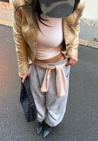 Beige leather jacket, white fitted top, grey sweatpants with pink waistband, holding a black woven bag, and wearing pointed black boots.