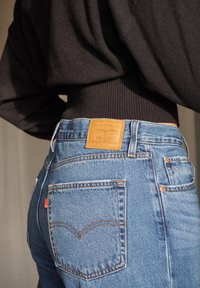 Jeans di denim azzurro chiaro con una toppa in pelle marrone sulla vita con la scritta "LEVI STRAUSS & CO.", e cuciture distintive sulle tasche posteriori.
