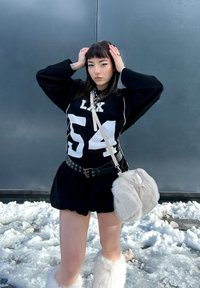 Top desportivo oversized preto com gráficos brancos, saia preta e acessórios de pêlo branco. Apresenta detalhes em metal prata numa cinta e numa bolsa.