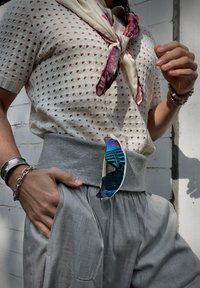 Könnyű, lyukacsos kötött felső, szürke, magas derekú nadrág és kék árnyalatú napszemüveg, beletűrve a nadrág derékpántjába.