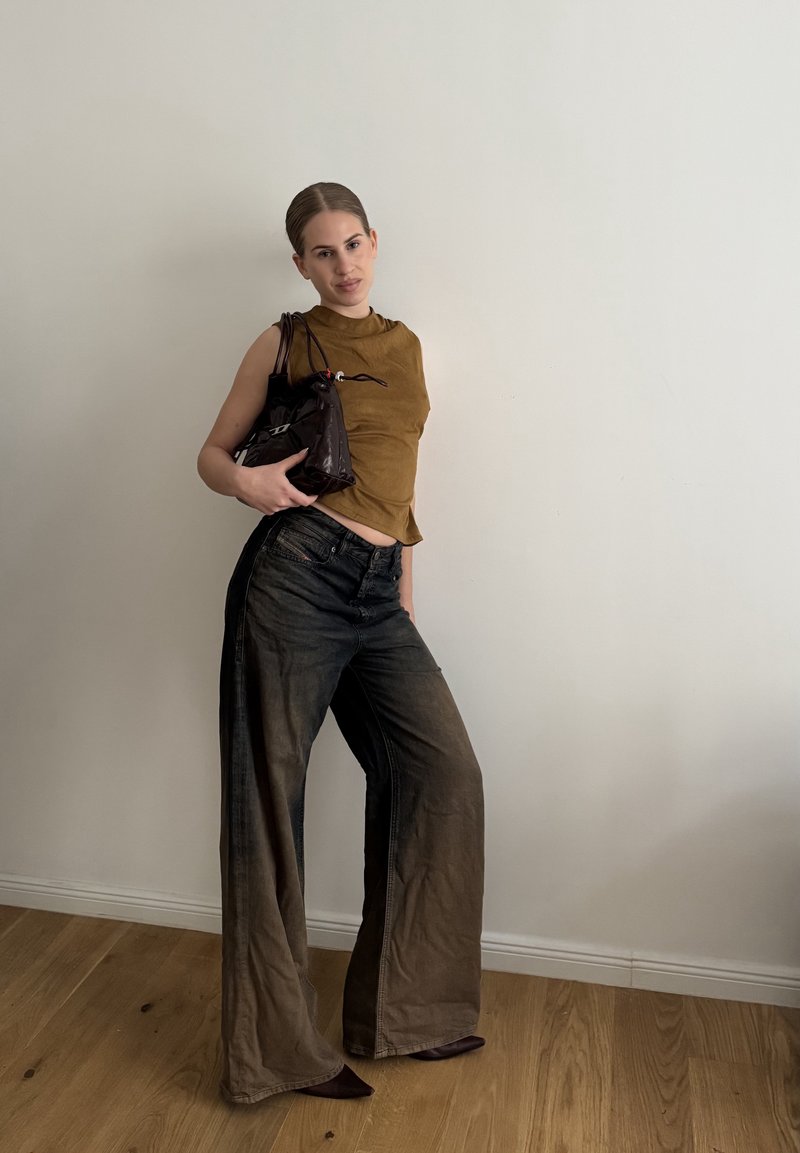 Brūns īsais bez piedurknēm tops, plata kāju izbalējuši melni džinsi un spīdīga melna rokassoma. Apģērbs izceļas ar vienmērīgu tekstūru un slāņotu dizainu.