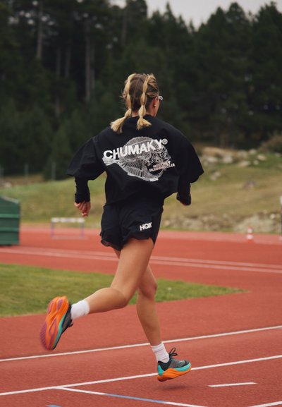 Corredor vestía una camiseta negra de gran tamaño con un diseño gráfico blanco y pantalones cortos negros, con zapatillas de correr coloridas, en una pista roja.