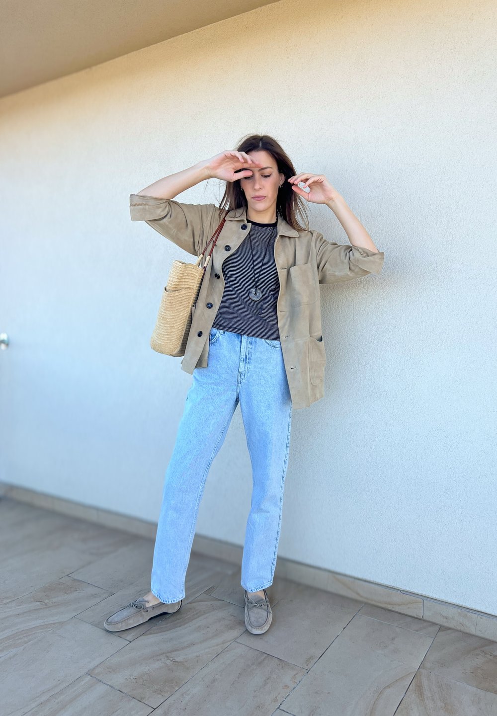 Μπεζ σουέτ τζάκετ πάνω από ένα μαύρο καρό πουκάμισο, ανοιχτό μπλε τζιν ψηλής μέσης και γκρι μπαλαρίνες. Τα αξεσουάρ περιλαμβάνουν μια πλεγμένη τσάντα.