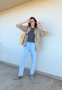 Μπεζ σουέτ τζάκετ πάνω από ένα μαύρο καρό πουκάμισο, ανοιχτό μπλε τζιν ψηλής μέσης και γκρι μπαλαρίνες. Τα αξεσουάρ περιλαμβάνουν μια πλεγμένη τσάντα.