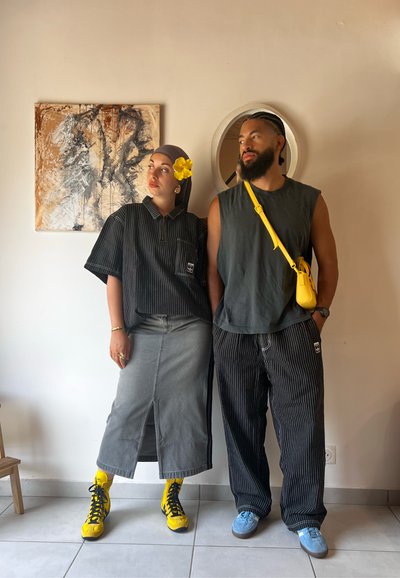 Conjuntos a rayas en negro y gris, botas amarillas y accesorios. Una persona lleva un pañuelo en la cabeza con una flor, la otra un bolso cruzado.