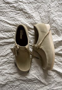 Beige semišové boty s kulatou špičkou, šněrováním a texturovanou podrážkou. Interiér nese branding "Clarks Originals" na tmavé stélce.