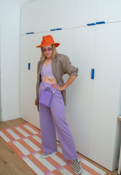 Pantalones de pierna ancha morados combinados con un crop top lavanda, un blazer marrón, un sombrero naranja y un bolso morado. Unos zapatos de lona con estampado de ajedrez completan el look.
