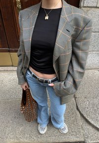 Blazer a quadri con tonalità grigio, nero e arancione, top nero aderente, jeans a campana blu chiaro, borsa marrone con borchie. Sneakers chunky.