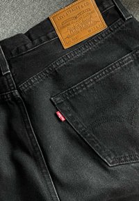 Μαύρα τζιν Levi’s που δείχνουν τη πίσω τσέπη, την κόκκ ινη ετικέτα Levi's και το δερμάτινο λογότυπο σε ταμπά χρώμα με μέγεθος W33 L32 στη ζώνη της μέσης.