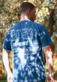 Marineblå bomulds T-shirt med stor hvid tekst på ryggen med forskellige sætninger og et lille grafisk mærke nær bunden. Korte ærmer.