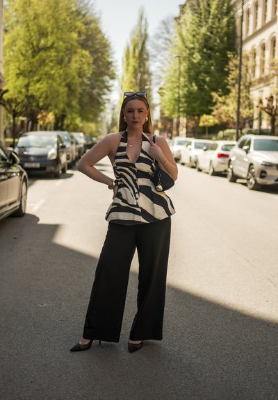 Pantalones anchos negros combinados con una blusa sin mangas de rayas en blanco y negro. El atuendo cuenta con un diseño de cuello halter y se complementa con tacones.