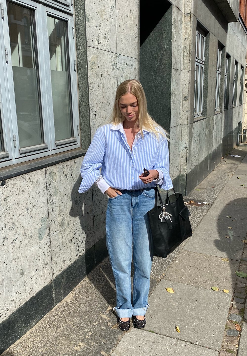Μπλε και άσπρη ριγέ πουκάμισο με υπερμεγέθη μανίκια, ανοιχτό μπλε τζιν με διπλωμένα μπατζάκια και μαύρη τσάντα ώμου. Παπούτσια με πουά.
